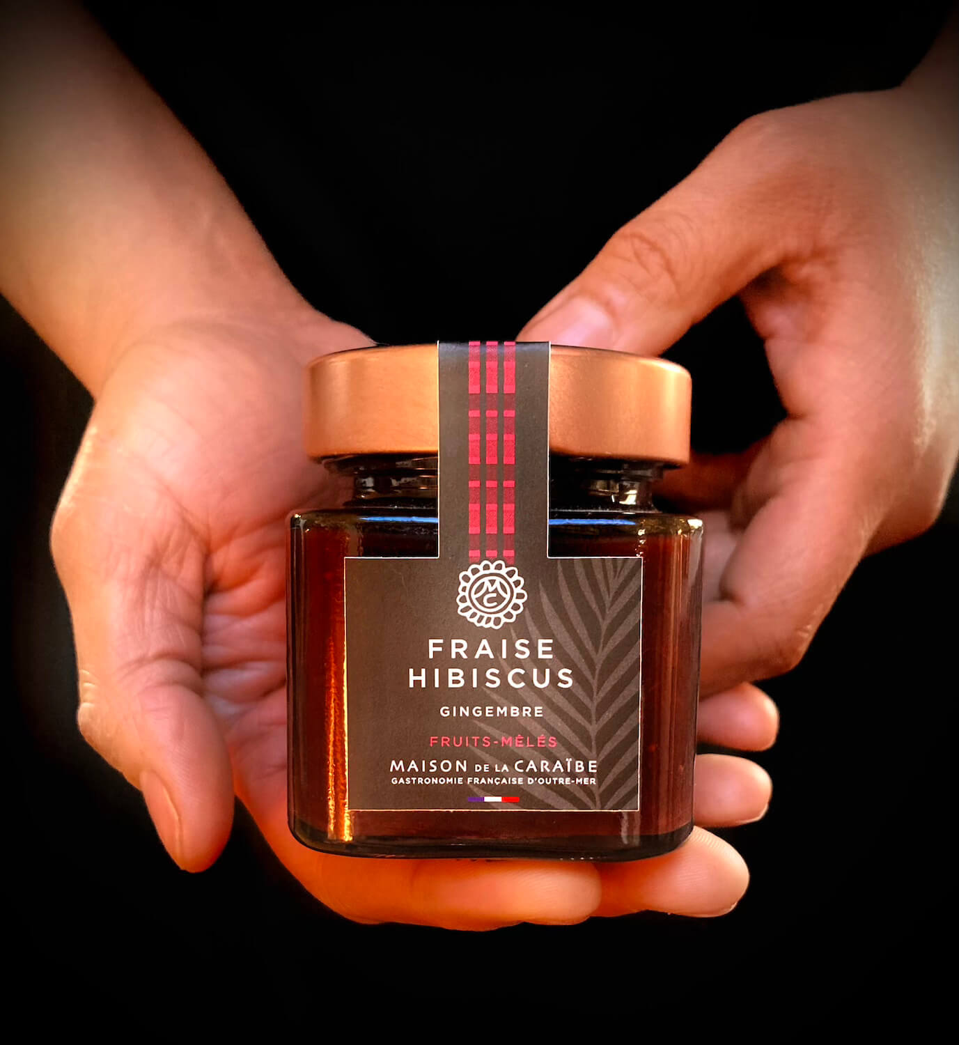pot de confiture de fraise et hibiscus tenu entre les mains d'une personne